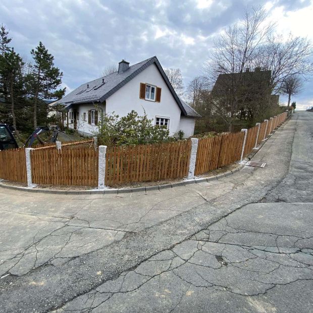 Zaunanlage mit grauen Granitsäulen und Staketenzaun.